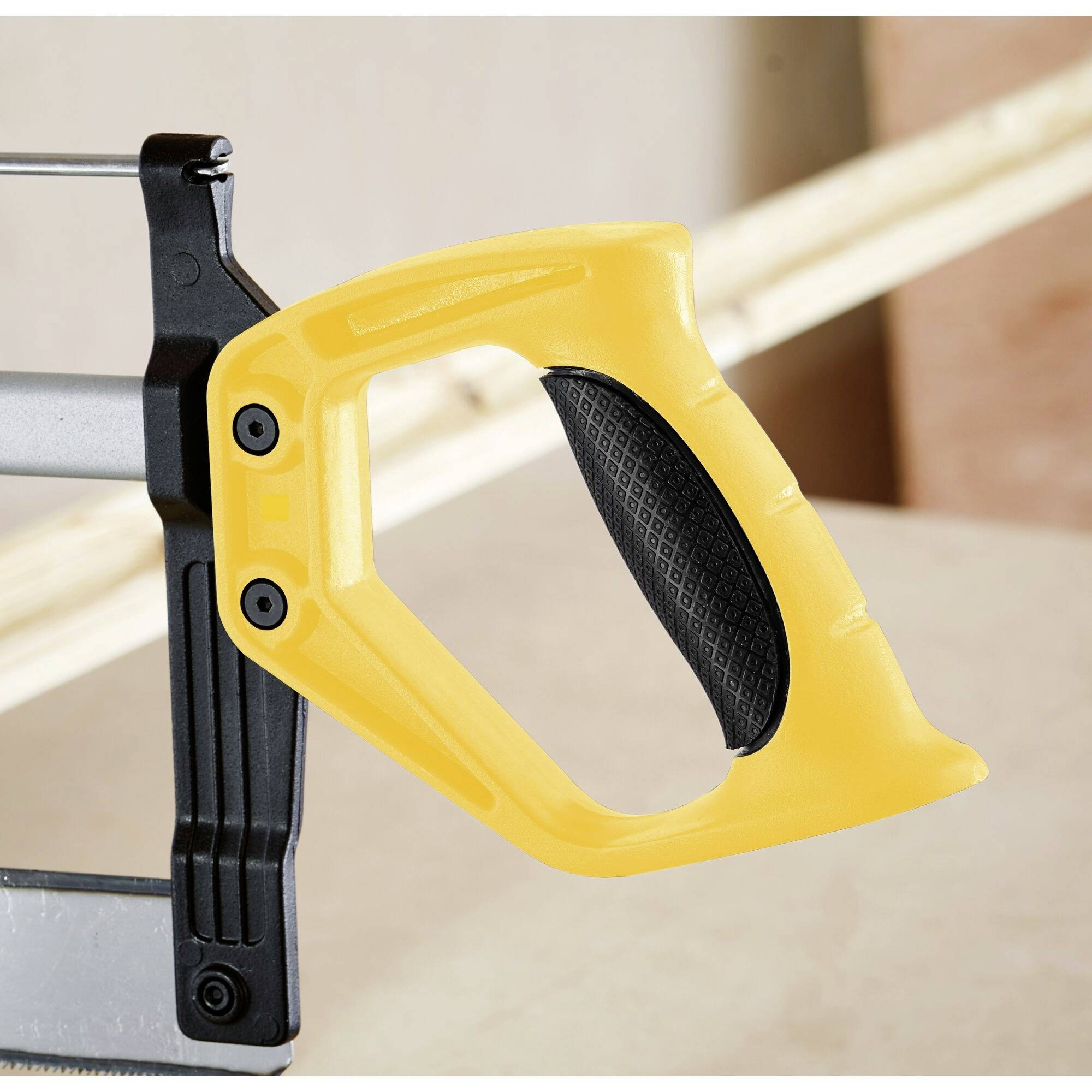 Een gele decoupeerzaag op een houten tafel. Het handvat is ergonomisch gevormd; op de achtergrond zijn houten balken zichtbaar.