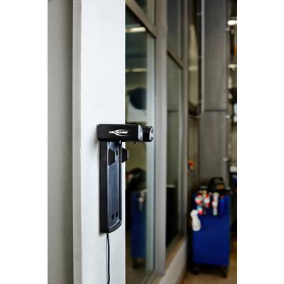Een zwarte laadstation voor elektrisch gereedschap is aan een muur bevestigd. Op de achtergrond staat een werkkar met verschillende gereedschappen.