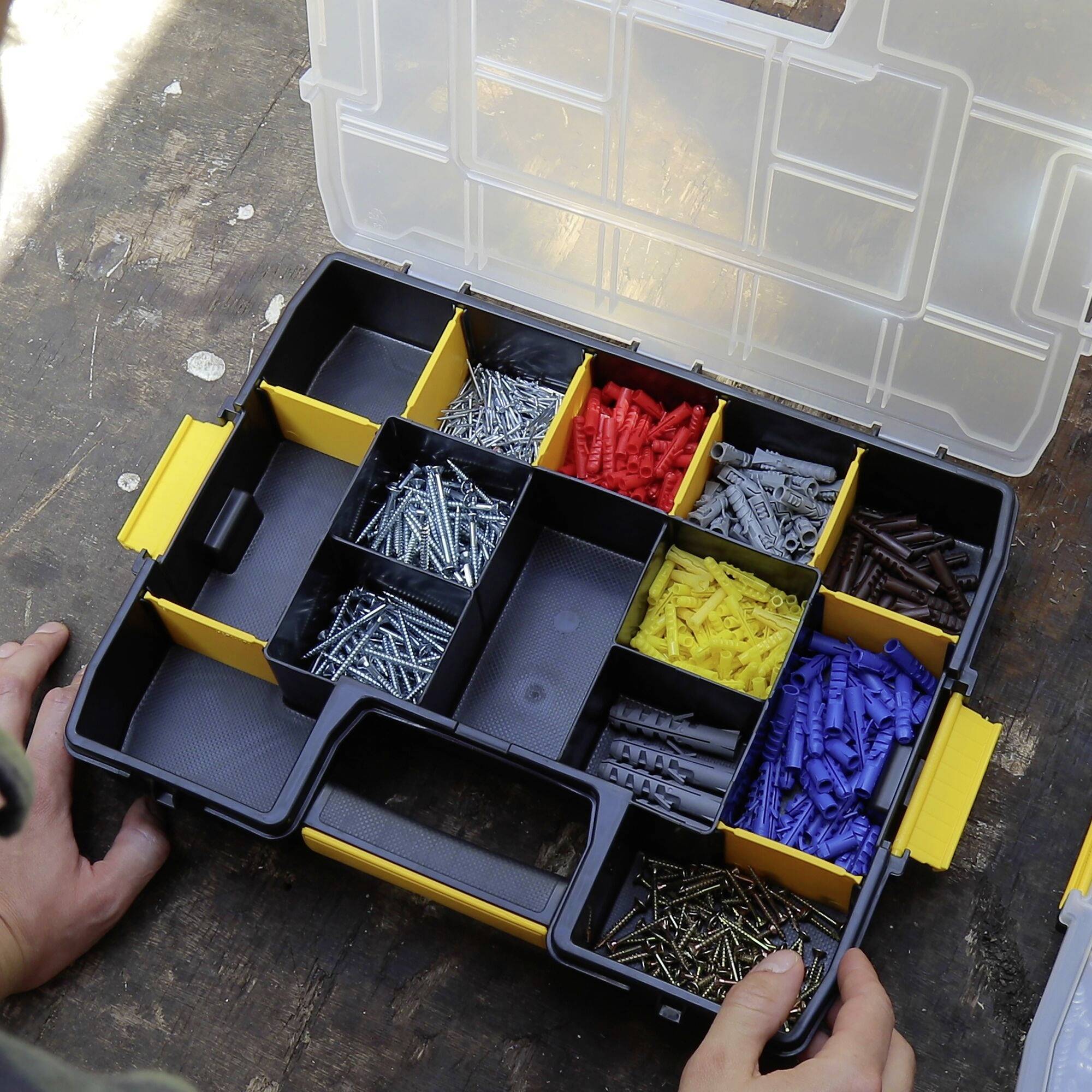 Een geopende plastic organizer op een tafel toont verschillende schroeven en pluggen in meerdere vakken, gerangschikt op kleur.