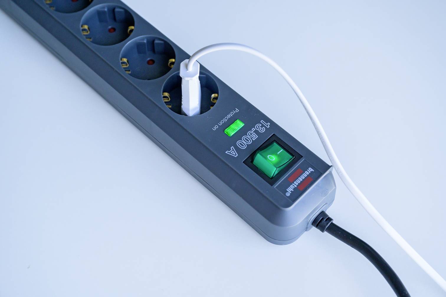 Een grijze stekkerdoos met een groene aan/uit-schakelaar, waaraan een zwart en een wit snoer zijn aangesloten.