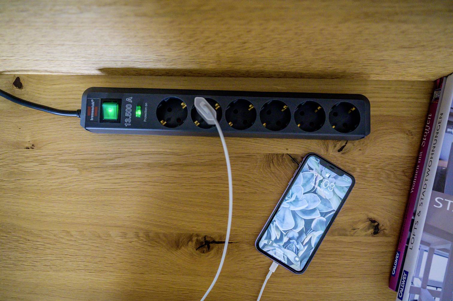 Een stekkerdoos met meerdere aansluitingen op een houten tafel. Een smartphone is erop aangesloten en wordt opgeladen.