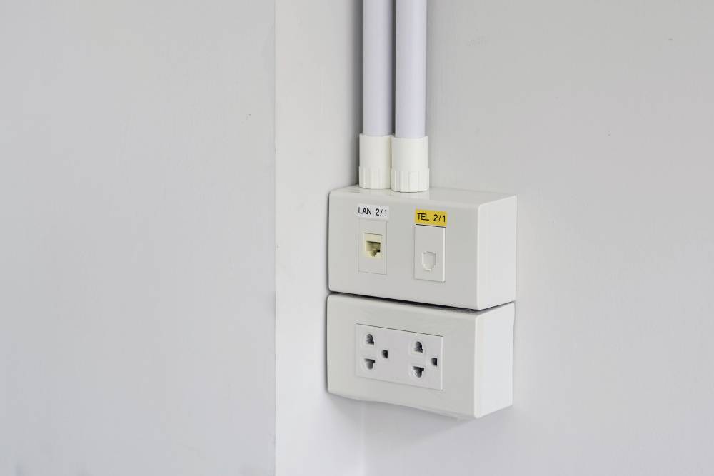 Een witte wandcontactdoos met twee driepins stopcontacten en netwerkaansluitingen, gemarkeerd met 'LAN 2/1' en 'TEL 2/1'.