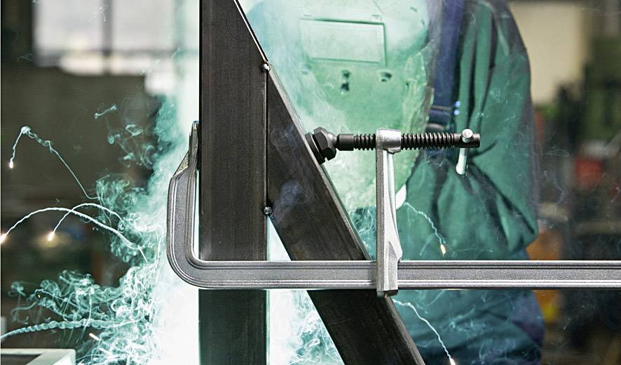 Een lasser in beschermende kleding werkt aan een metalen frame. Vonken vliegen rond terwijl hij metaal aan elkaar last met een lasapparaat.