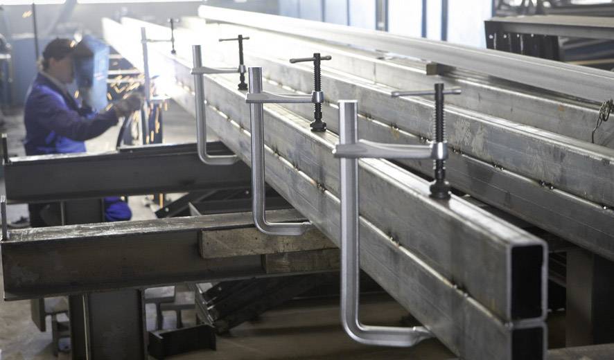 Een persoon last in een werkplaats, metalen werkstukken zijn met klemmen vastgezet en op een rij gezet; werkproces in de metaalbewerking.