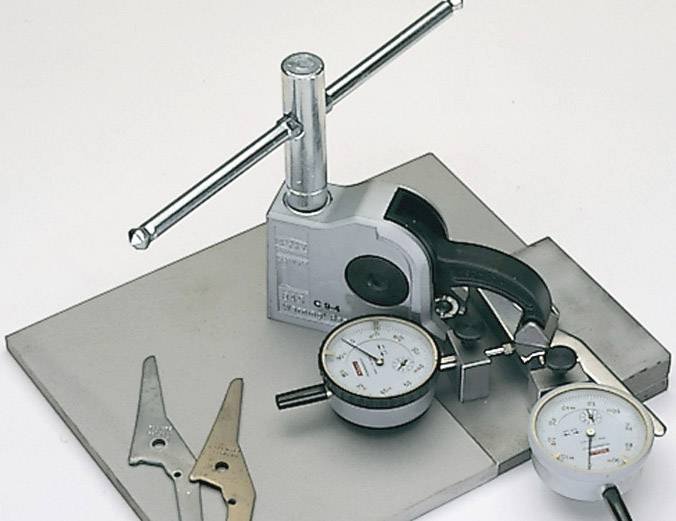 Manometers op een metalen plaat voor het meten van druk. Ernaast liggen metalen onderdelen en een hefboom die de meting ondersteunen.