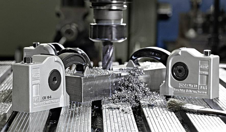 Een freesmachine bewerkt een metalen werkstuk, omgeven door vier magneetspanners, met metaalspanen op een machinale werktafel.