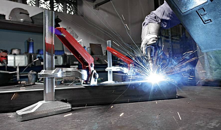 Een persoon last aan een metalen stuk terwijl vonken rondvliegen. Op de achtergrond zijn gereedschappen en werkbanken te zien.