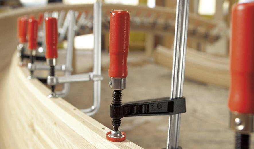 Verschillende klemmen met rode handgrepen houden houten planken stevig op hun plaats in een werkplaats.