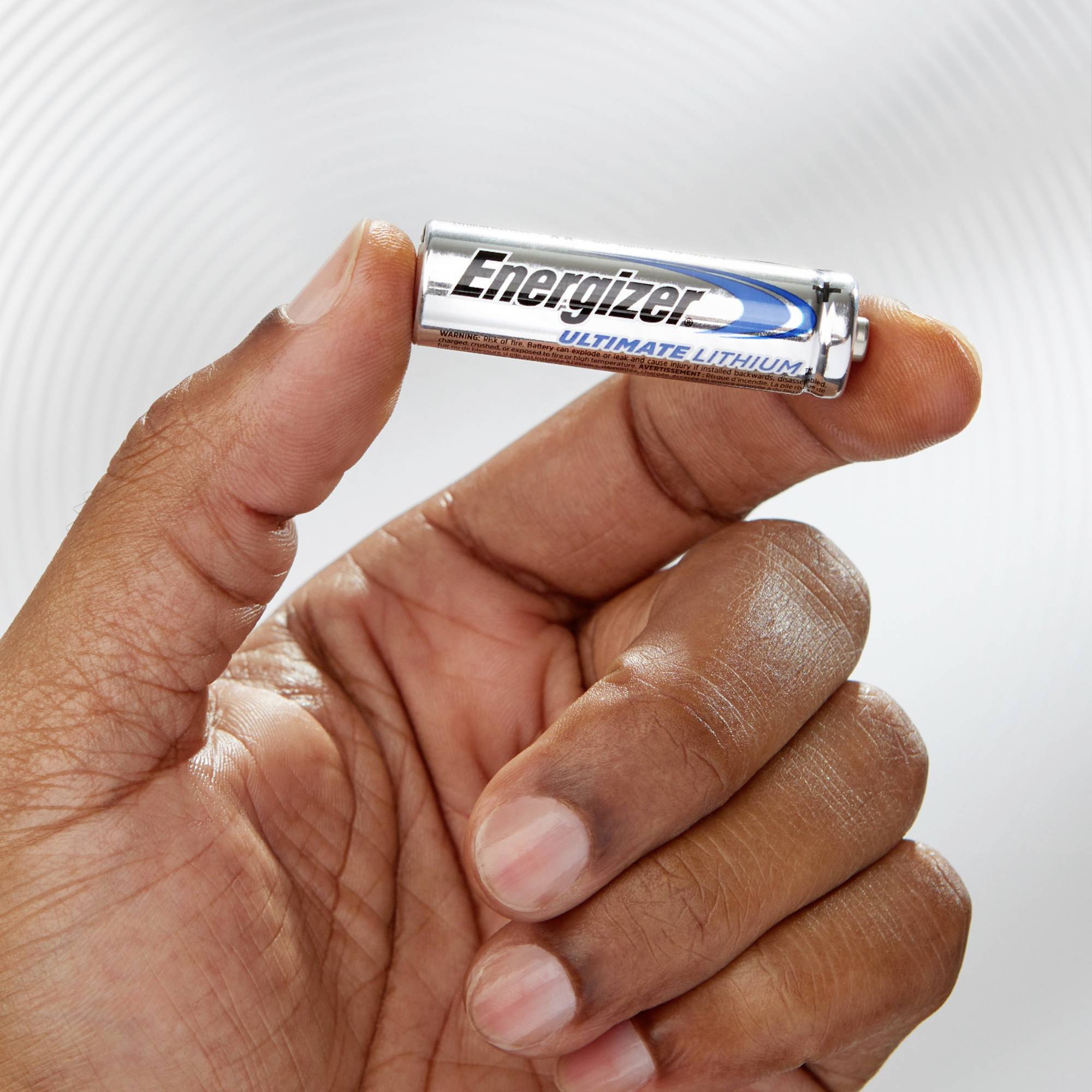 Een hand houdt een zilveren AA-batterij met het opschrift 'Energizer Ultimate Lithium' tegen een neutrale achtergrond.