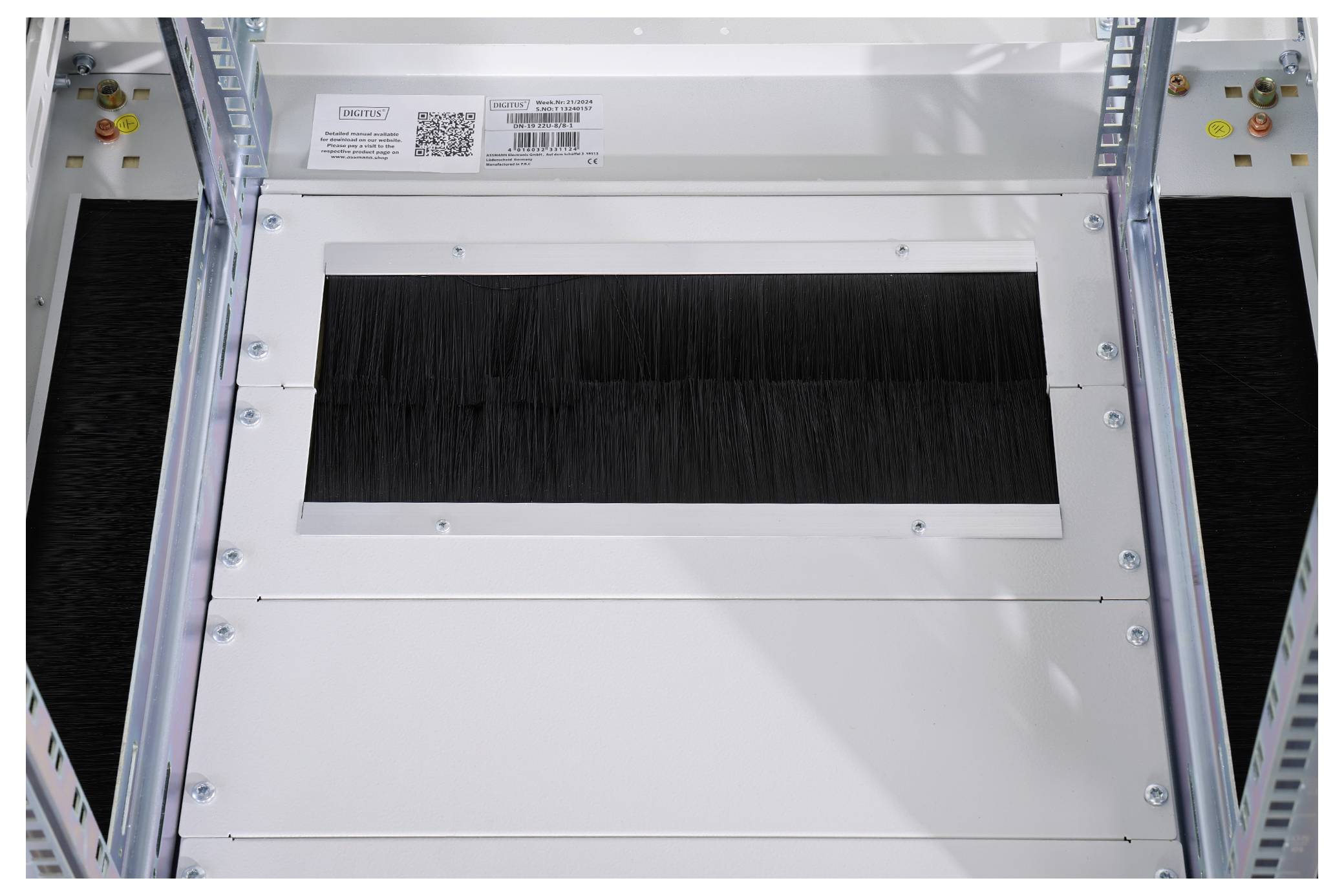 Een wit metalen behuizing met rechthoekige uitsparing, omringd door schroeven. Bovenaan een etiket met QR-code en meertalige tekst.