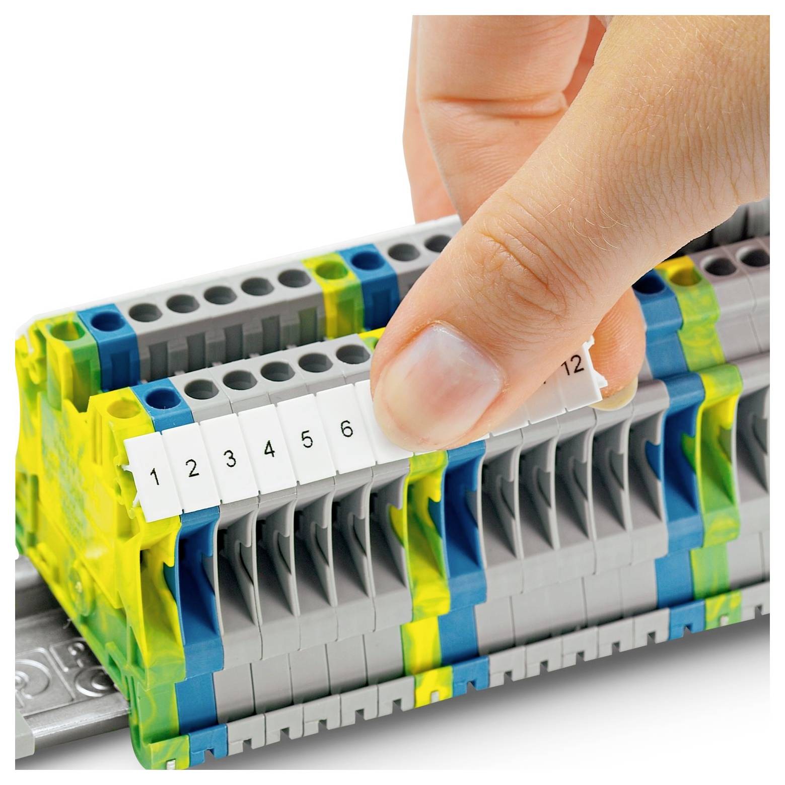 Een hand stelt genummerde labels op een elektrische klemmenblok in, die aansluitingspunten in een bedieningspaneel-opstelling aangeven.