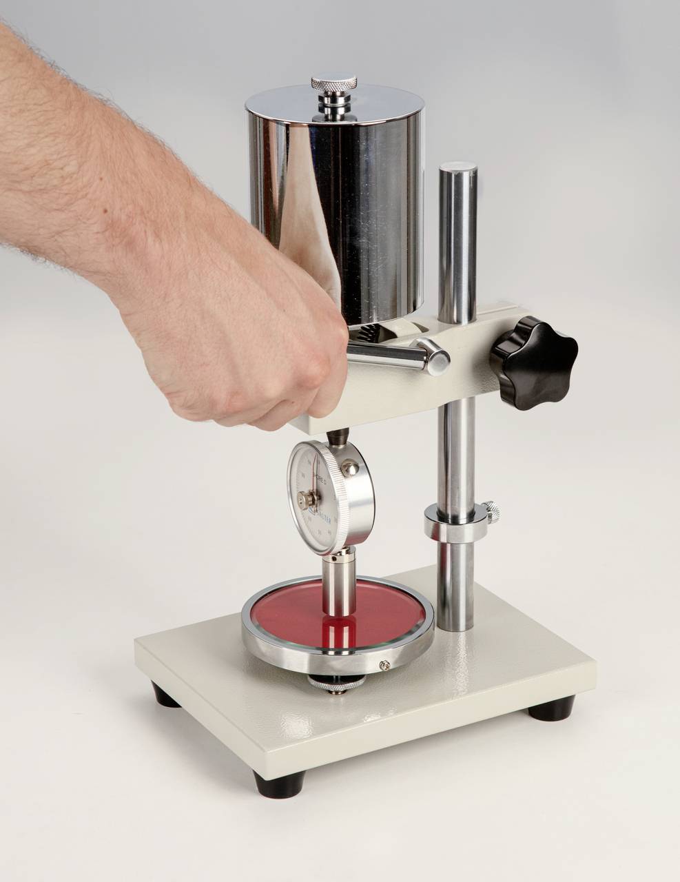 'Hand bedient een meetinstrument met metalen zuiger en schaal. Het apparaat staat op een stabiele voet en toont precisie bij gebruik.'