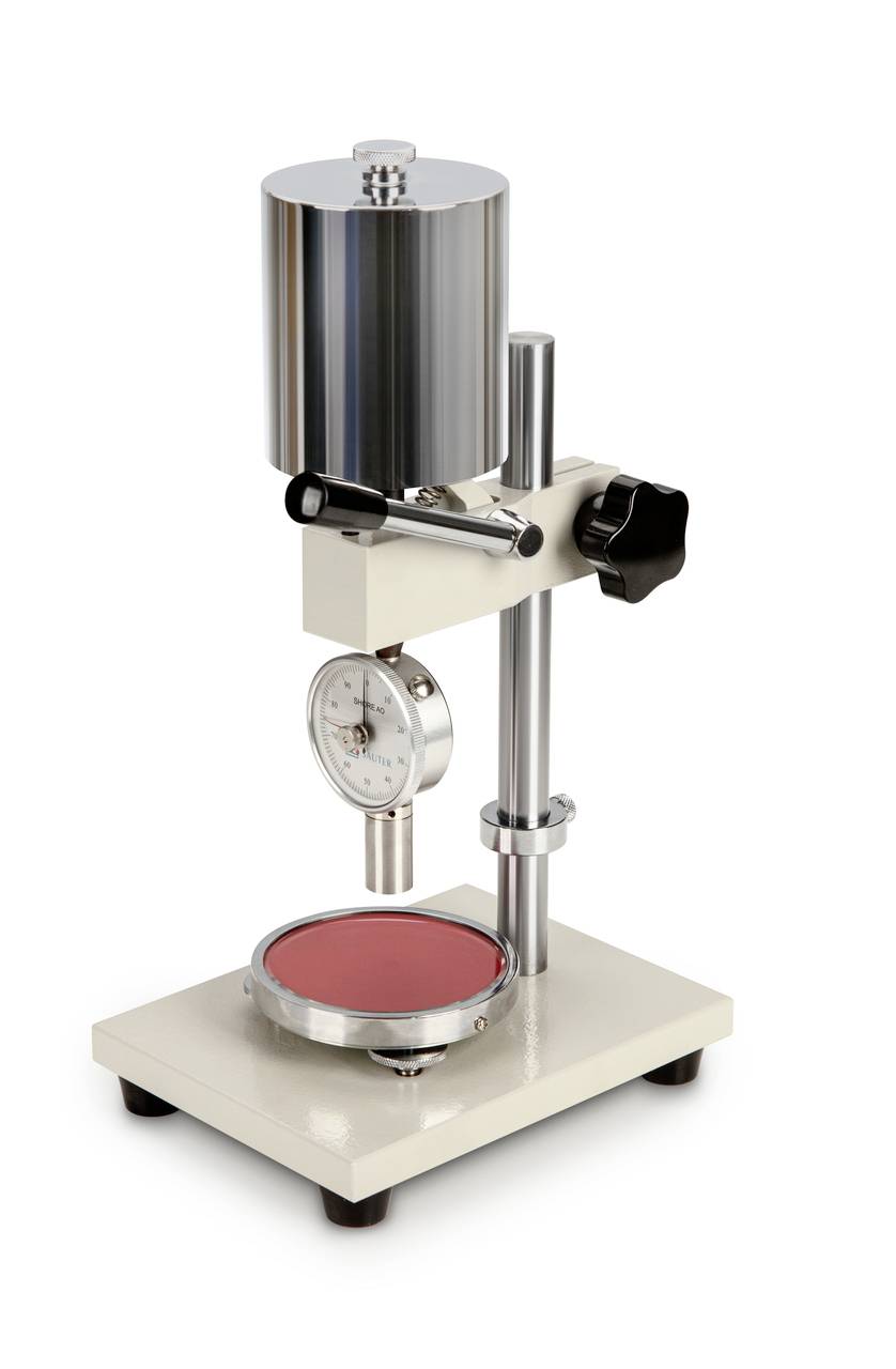 Een durometer-testapparaat voor het meten van de hardheid van materialen, met een rond rood monster op de basis.