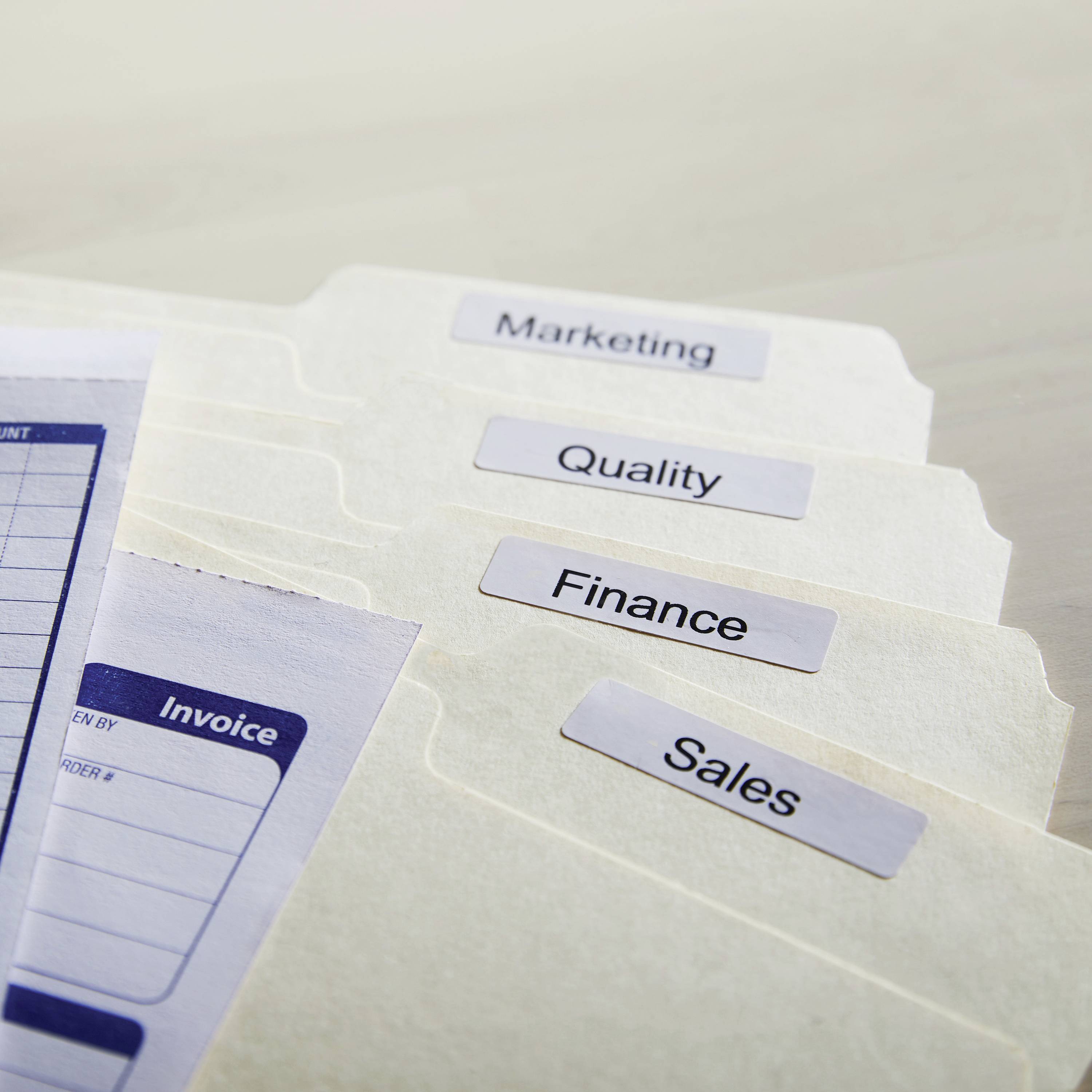 Ordnerregister met de labels 'Marketing', 'Quality', 'Finance' en 'Sales' op een bureau.