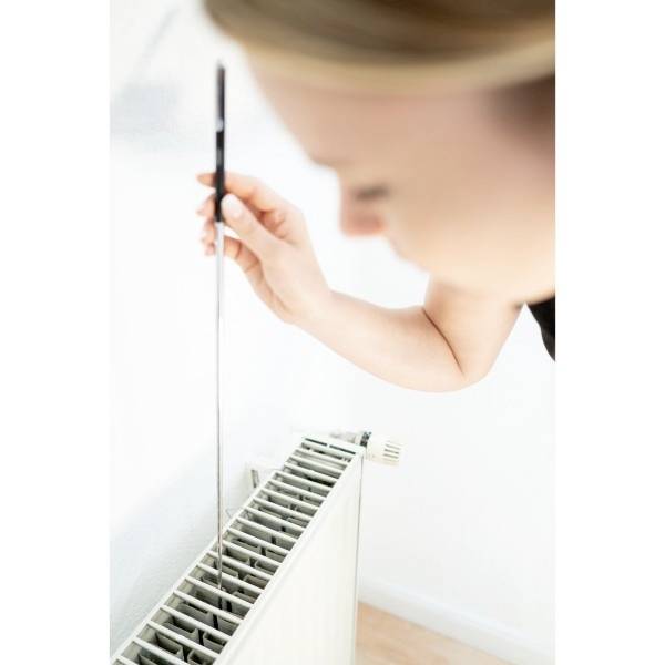 Een persoon ontlucht een radiator met een ontluchtingssleutel. De radiator bevindt zich aan een witte muur.