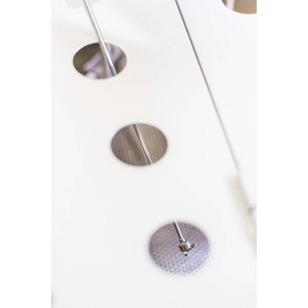 'Drie ronde openingen in een wit oppervlak, met onderliggende metalen elementen en een radiaal patroon.'