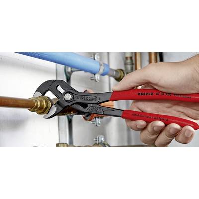 Een hand houdt een rode waterpomptang vast die een buis in een installatiesysteem vastklemt.