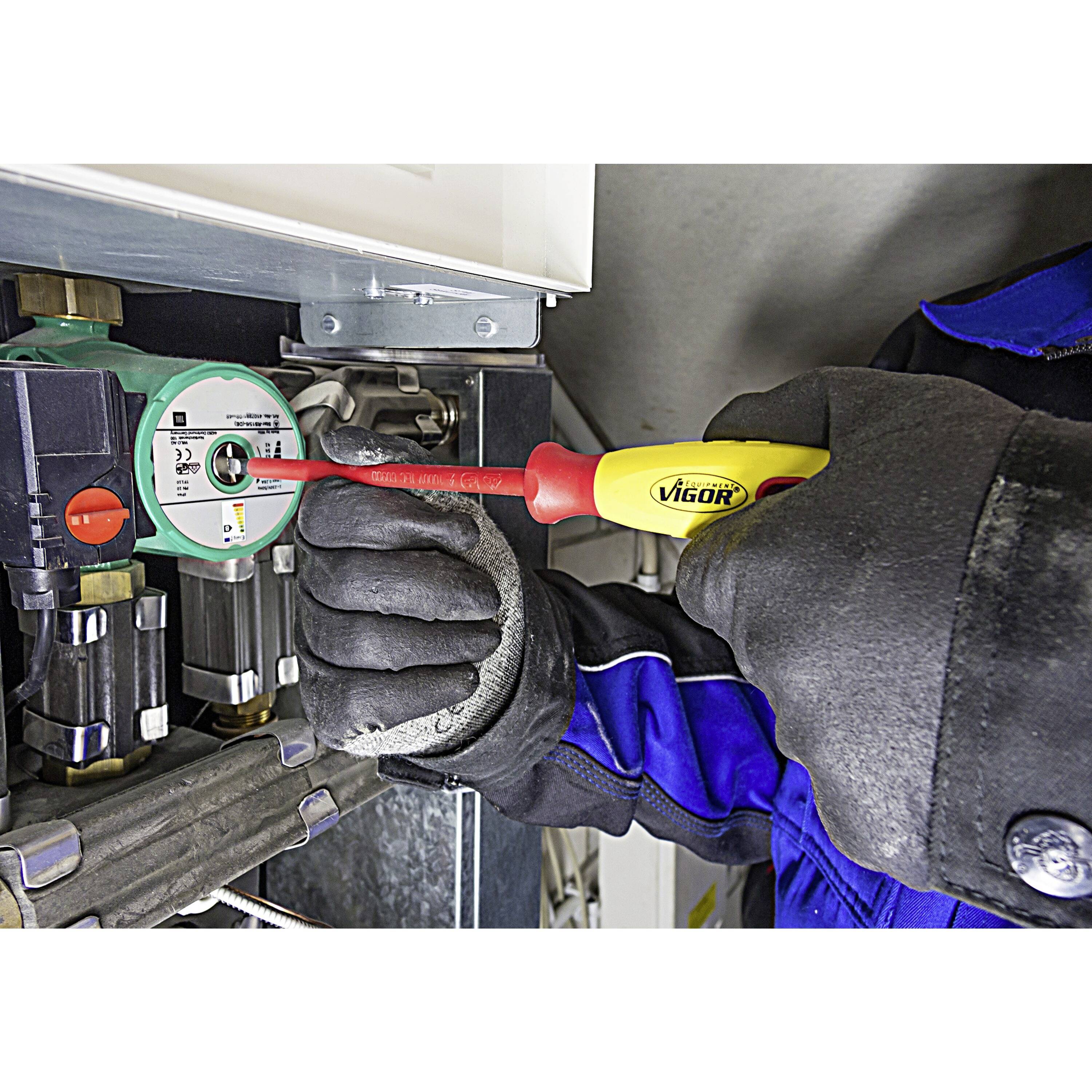 Een persoon die een schroevendraaier gebruikt op een groen en wit machineonderdeel, gekleed in handschoenen en blauwe werkkleding, als onderdeel van technisch onderhoud van apparatuur.