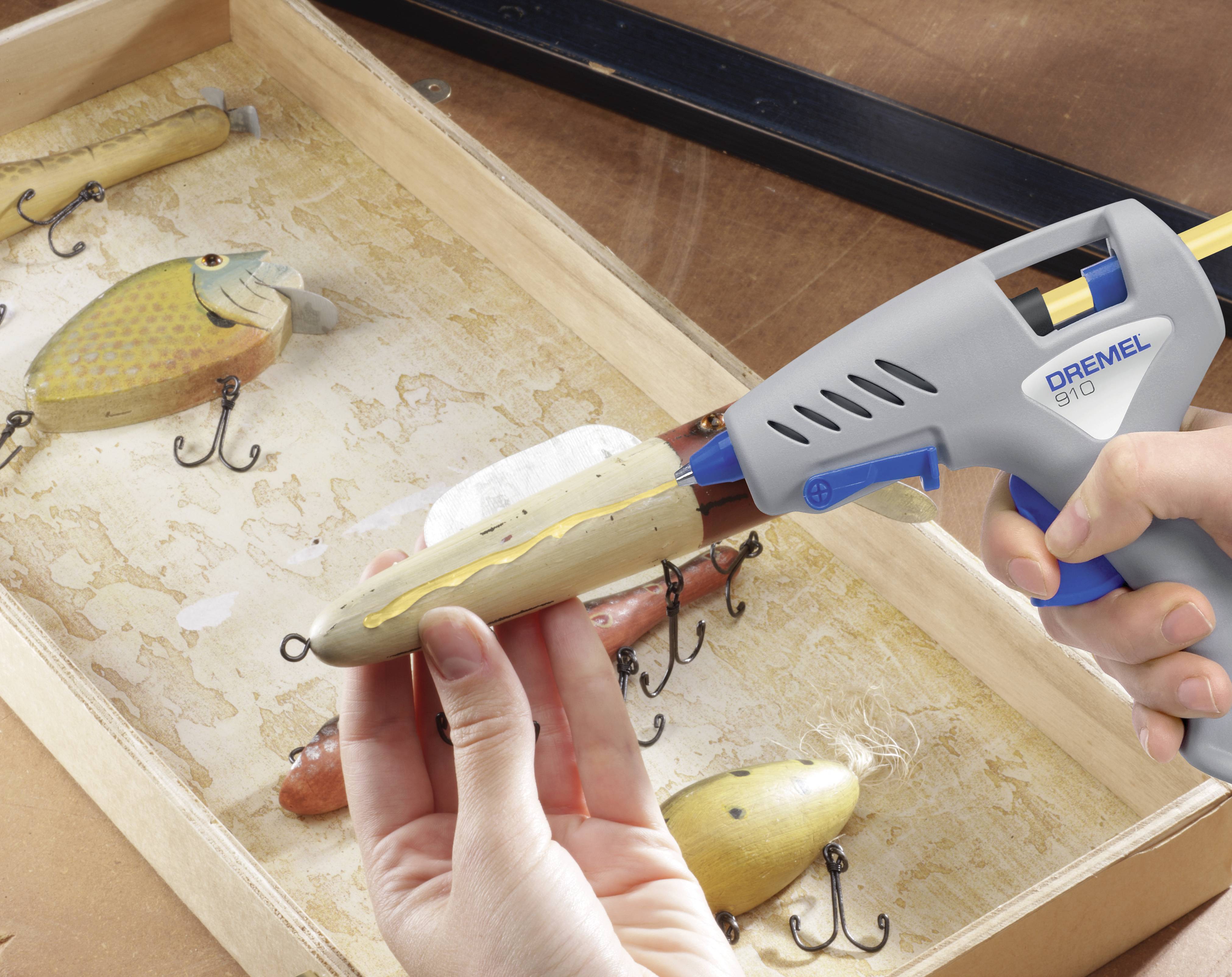 'Een persoon bevestigt een kunstaas met een lijmpistool op een houten oppervlak. Op de achtergrond zijn nog meer kunstazen zichtbaar.'