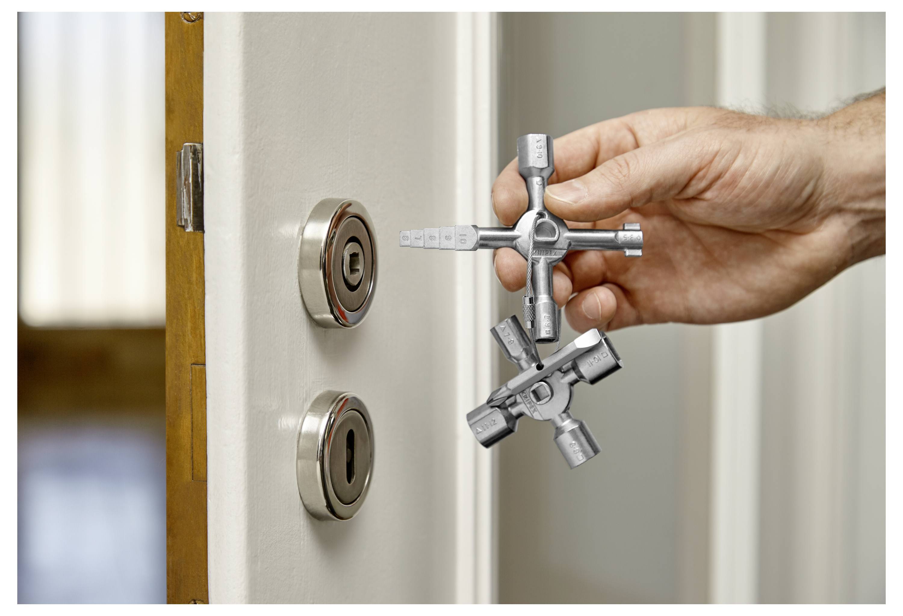 Een hand houdt een multifunctionele sleutel dicht bij een deur met twee sloten, wat op gebruik of installatie duidt.