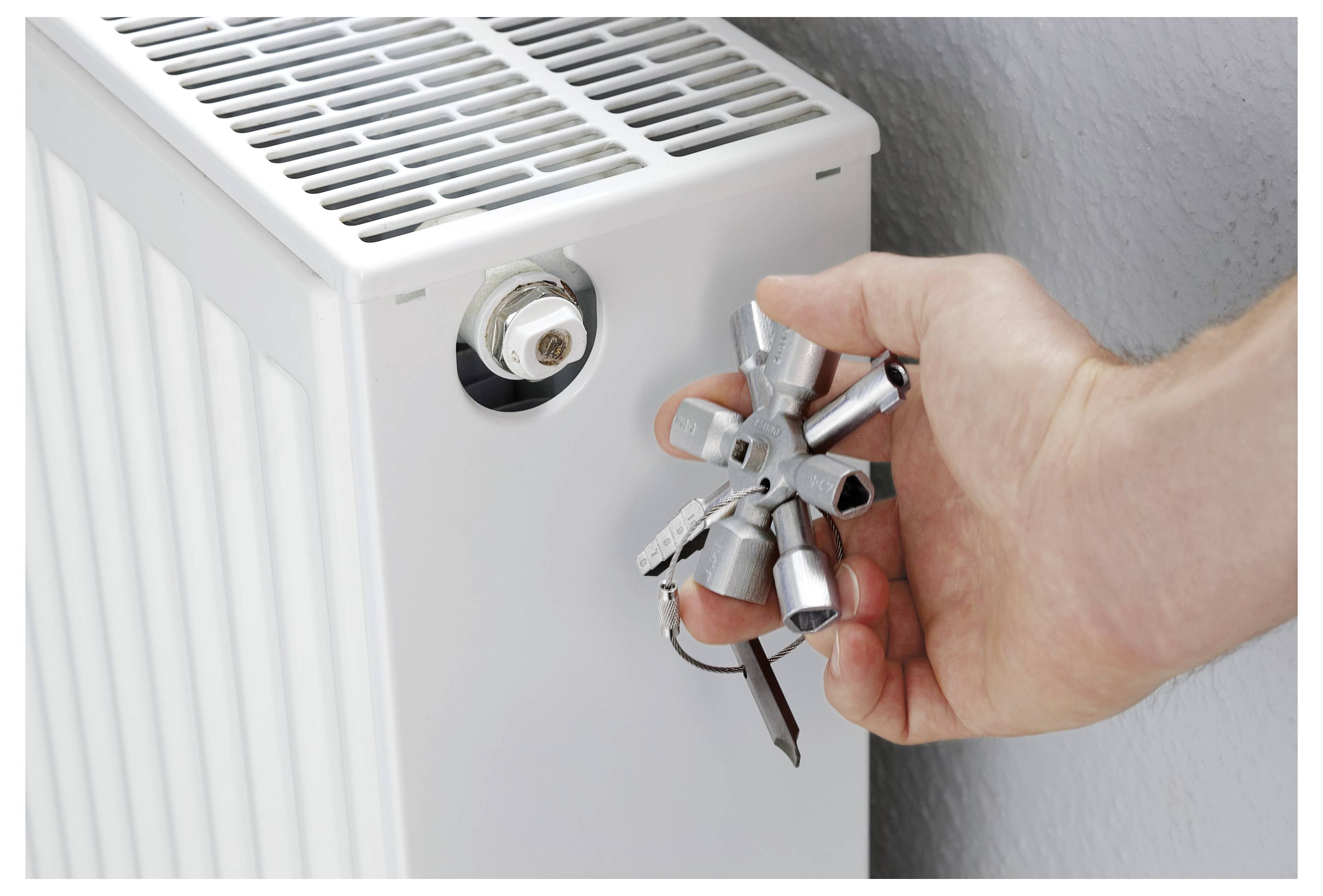 'Een persoon gebruikt een radiateursleutel om een radiator te ontluchten, wat zorgt voor betere verwarmingsefficiëntie.'