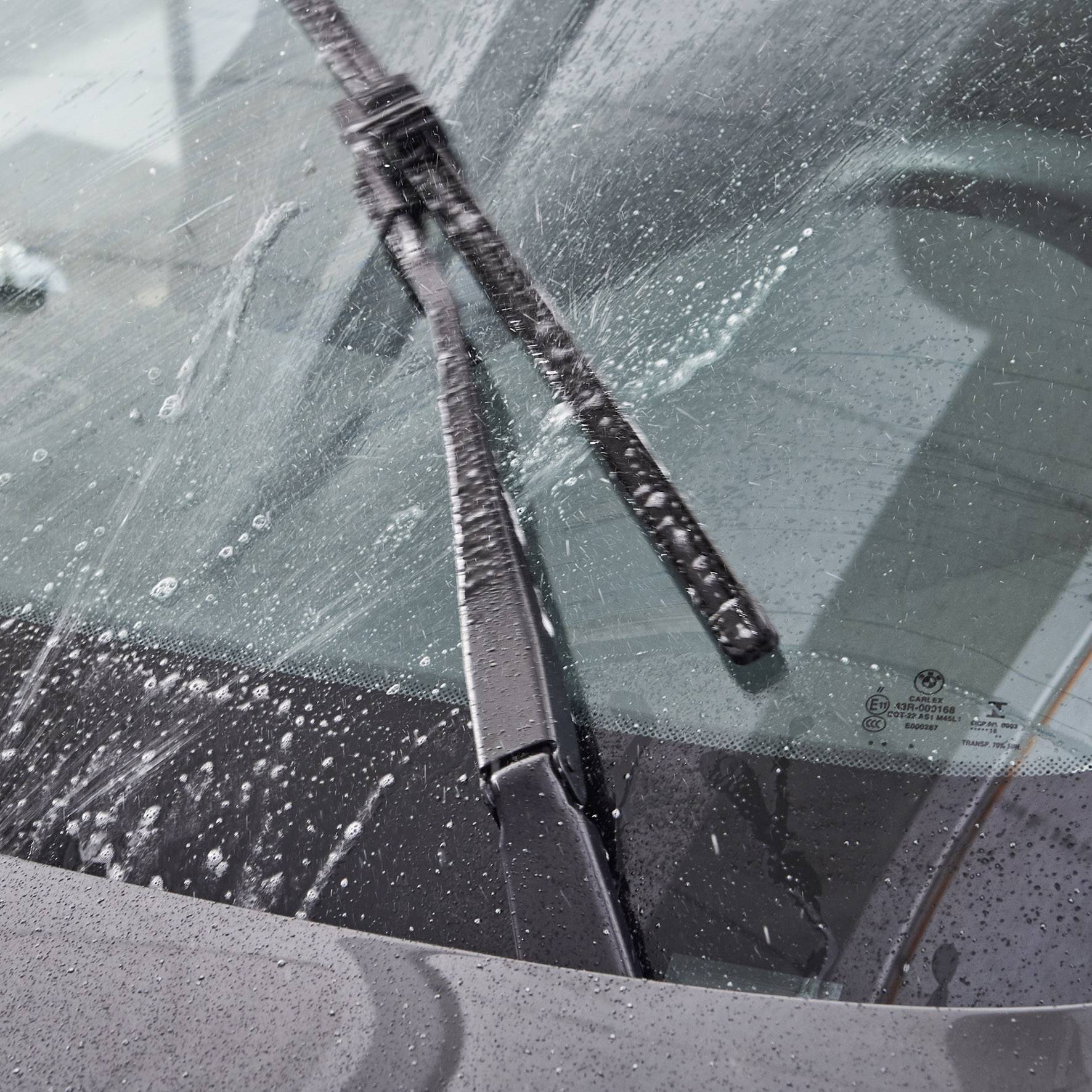 De ruitenwisser van een auto veegt over de voorruit tijdens motregen en laat heldere strepen na in het water en de schuimlaag.