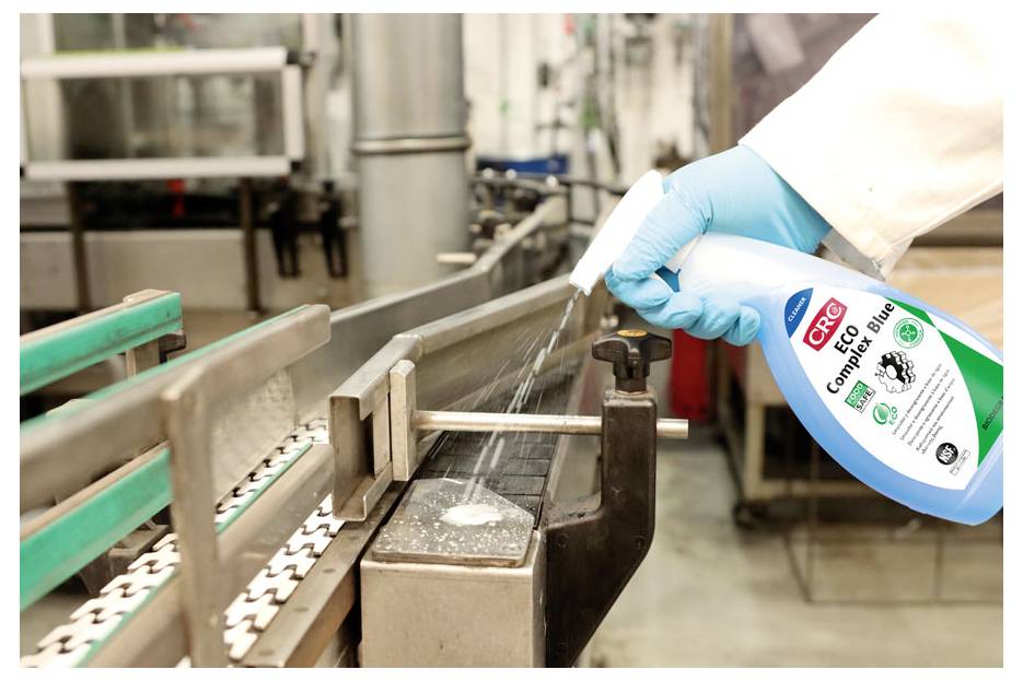 Een persoon met blauwe handschoenen spuit 'CRC Contact Cleaner' op een transportband in een industriële omgeving, wat wijst op onderhoud of reiniging.