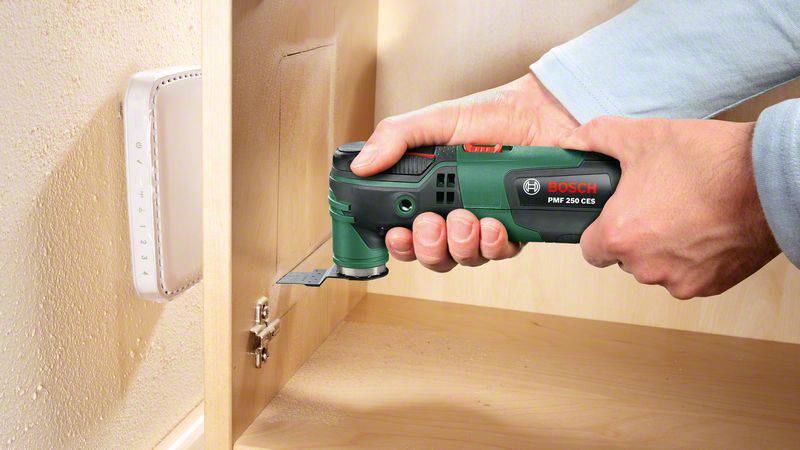 Een persoon houdt een oscillerend multifunctioneel gereedschap van Bosch tegen een houten kast. Het gereedschap bewerkt een klein oppervlak.