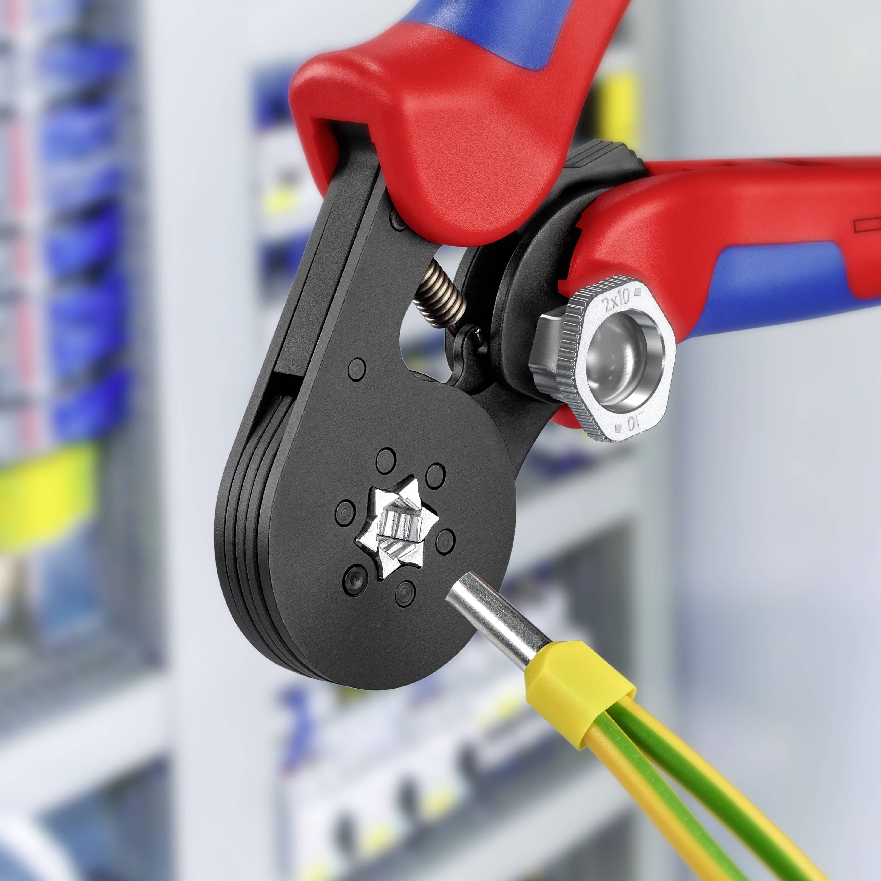Een rode en blauwe krimptang bevestigt een geel-groene elektrische adereindhuls in een werkplaats.