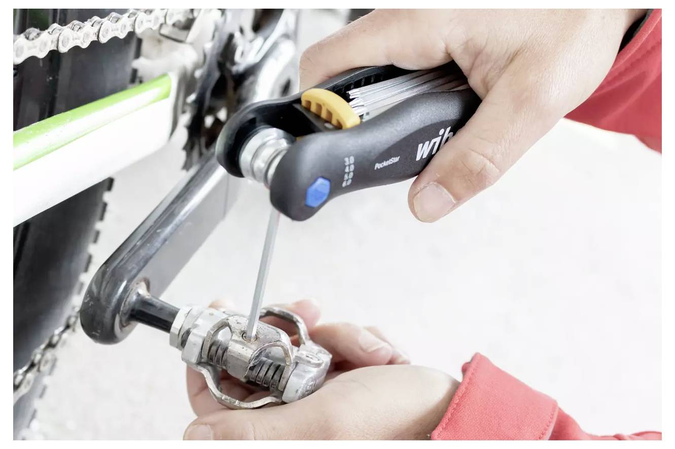 'Persoon stelt fietspedaal in met een multitool.'