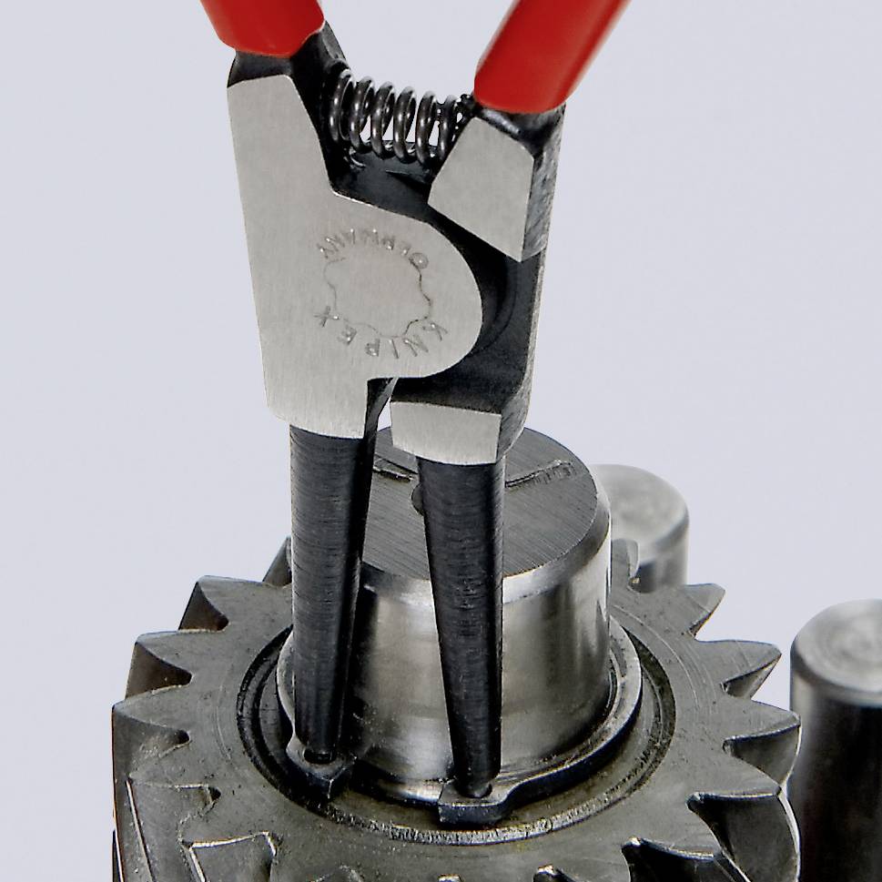 Een tang houdt een moer vast op een tandwiel, symboliseert mechanische precisie.