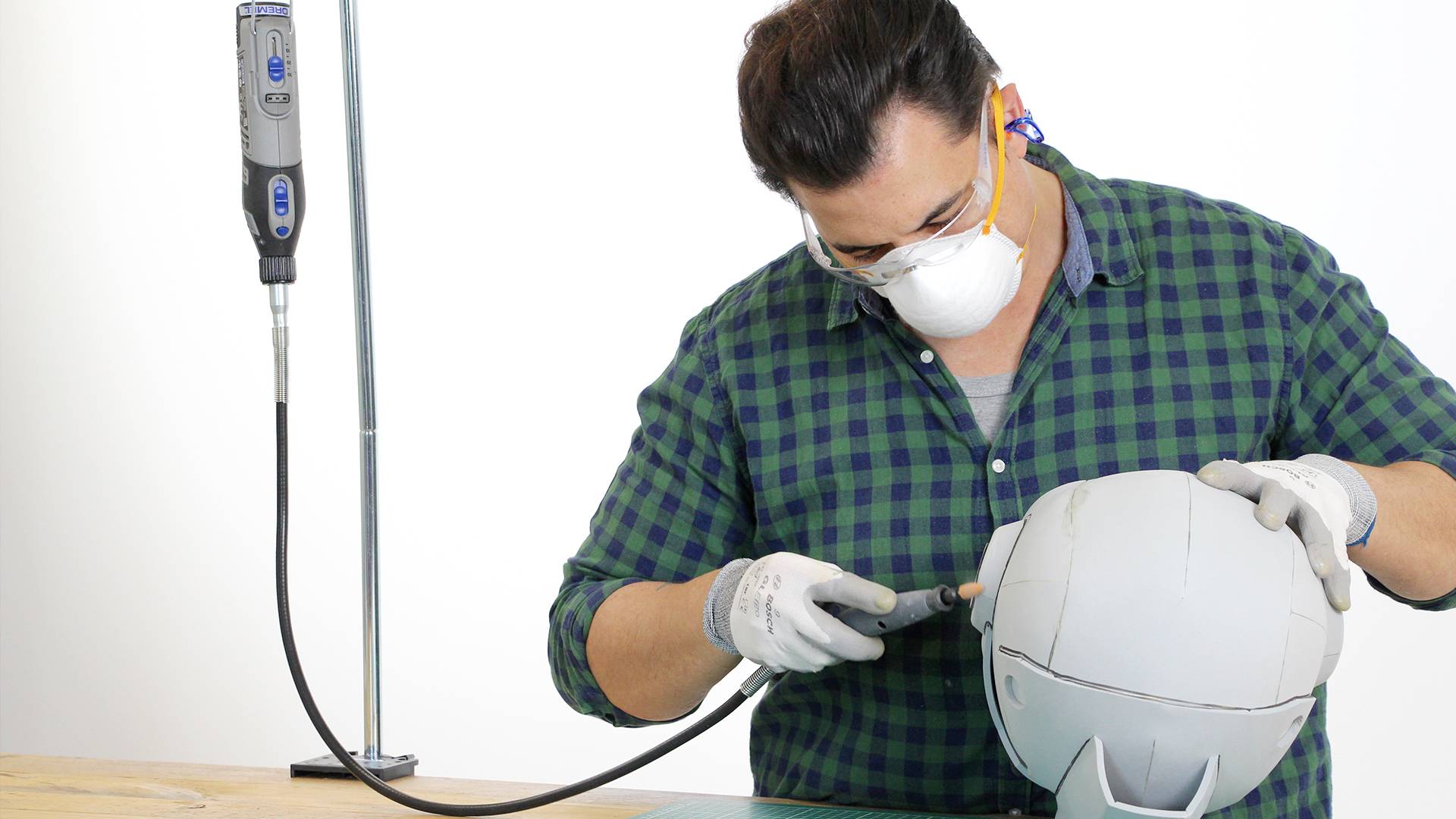 Een persoon met veiligheidsbril en masker bewerkt met een gereedschap een helm op een tafel.