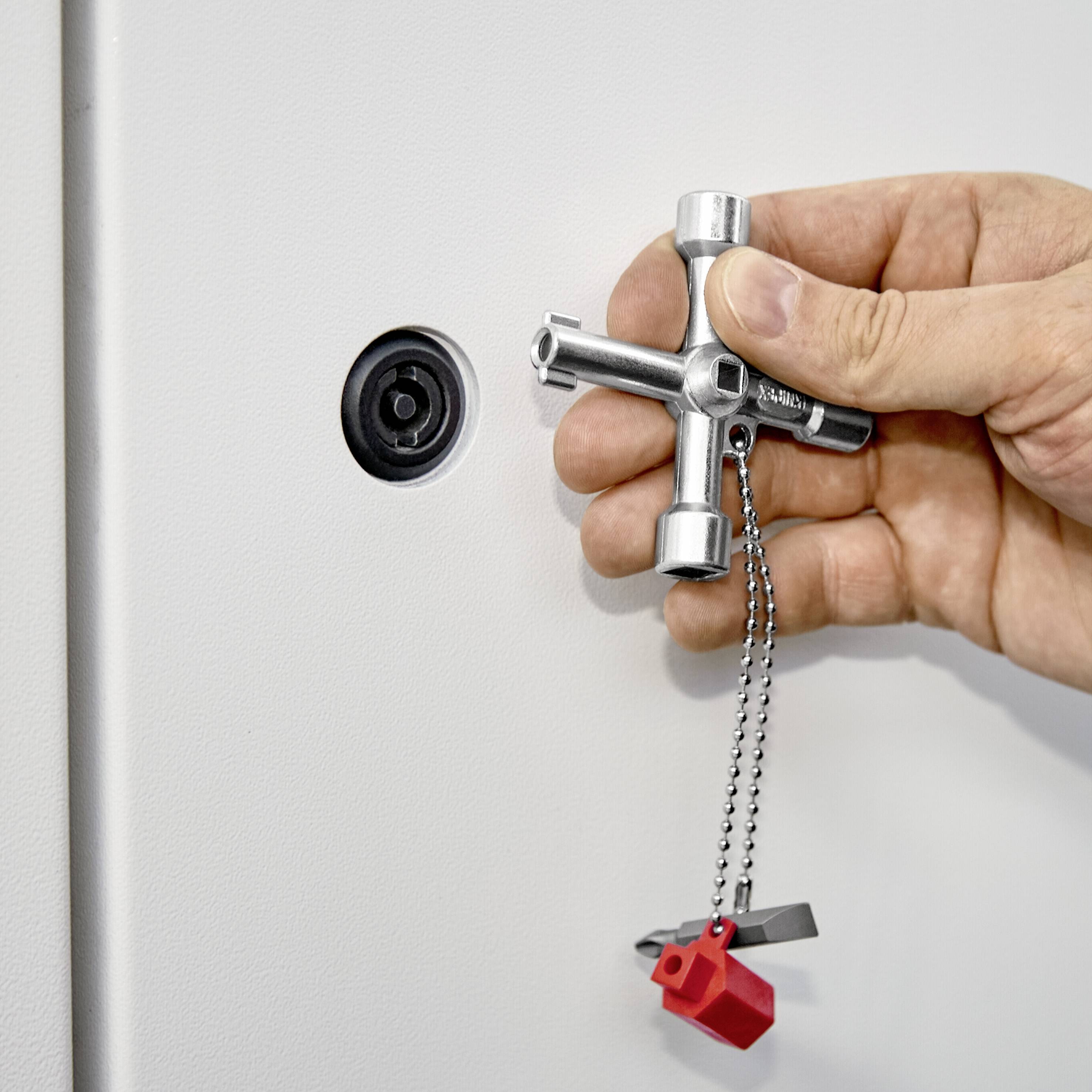 Een hand houdt een kruissleutel vast om een kluisje te openen. De sleutel hangt aan een ketting met een rode plastic hanger.