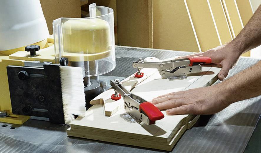 Machine in werkplaats met veiligheidsvoorziening, bediener legt houten stuk onder freesmachine voor precisiebewerking.