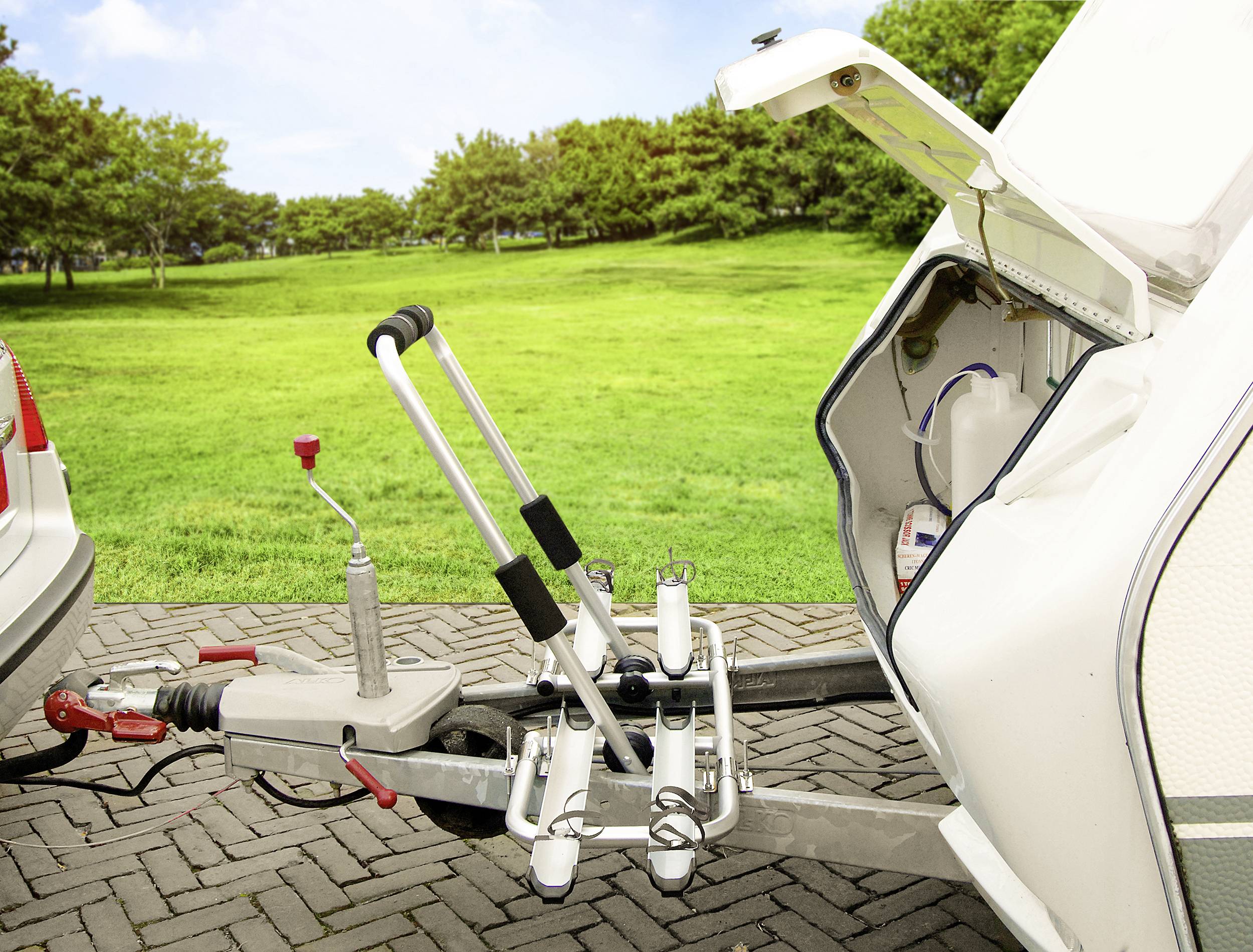 Een caravan is gekoppeld aan een auto. De bagageruimte van de caravan staat open. Op de achtergrond is een groene weide.