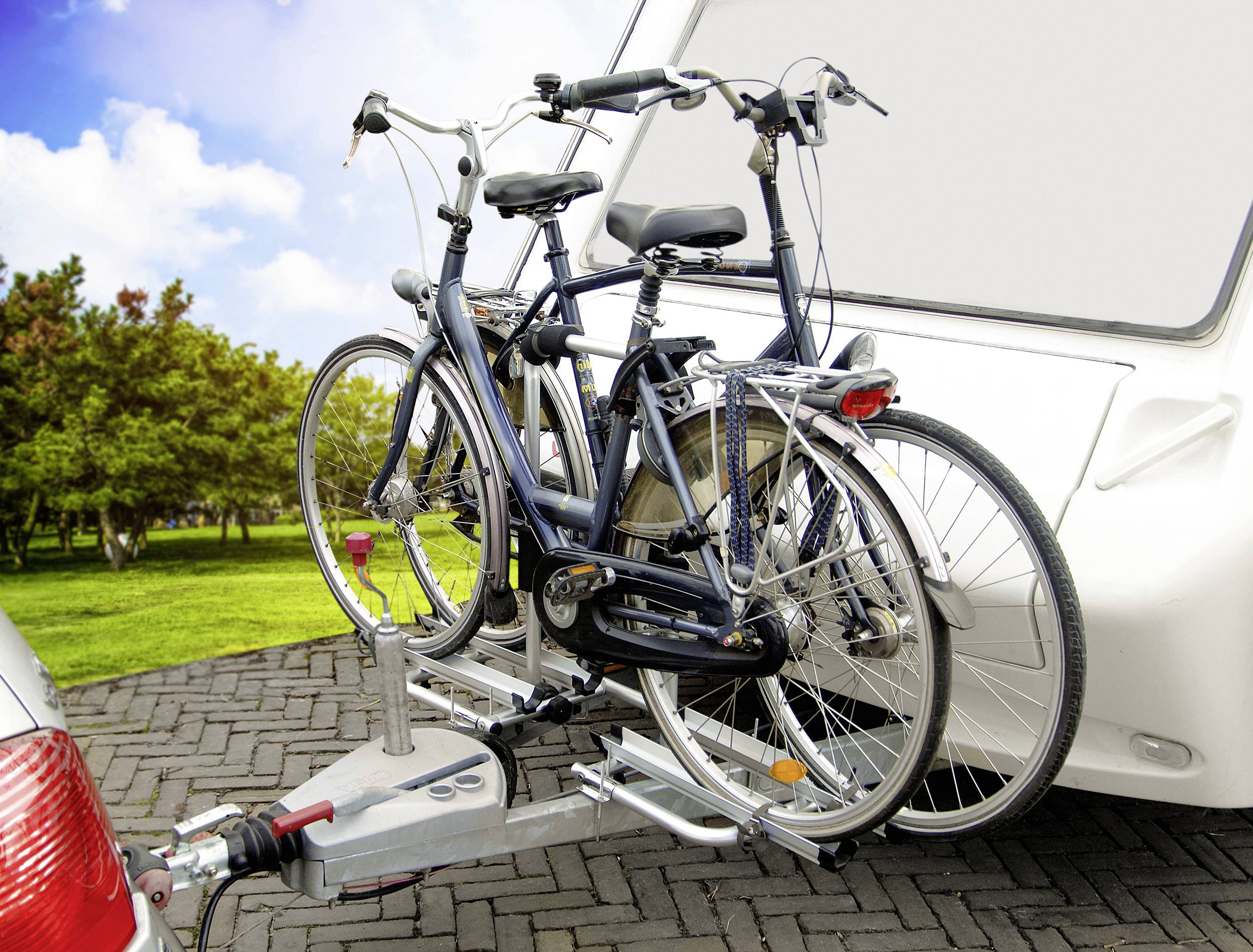 Twee fietsen zijn gemonteerd op een fietsendrager die aan een aanhangwagen is bevestigd. Op de achtergrond zijn bomen en een blauwe lucht.