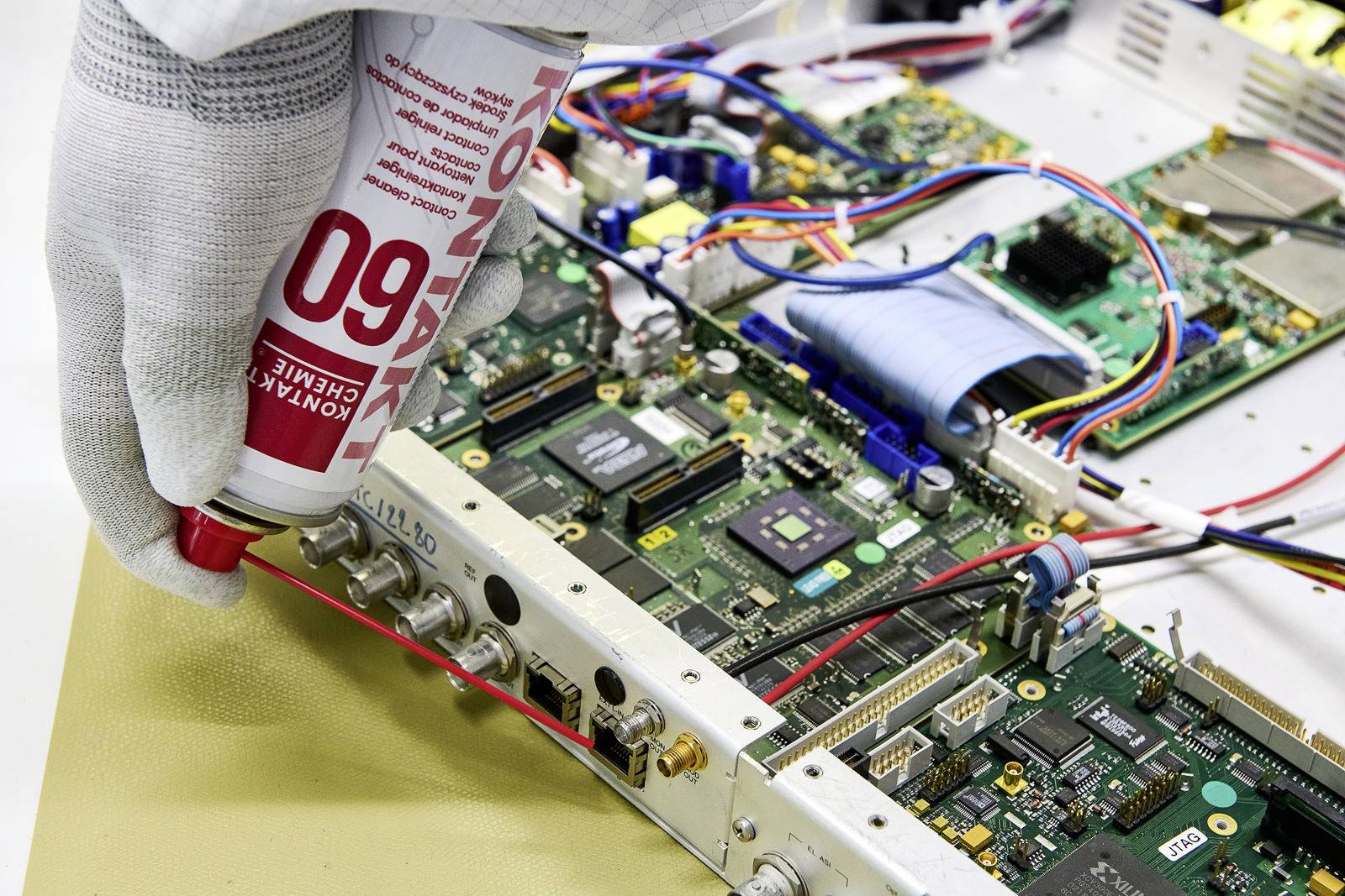 Een hand in een handschoen brengt thermische pasta aan op elektronische componenten in een apparaat om de warmteafvoer te verbeteren.