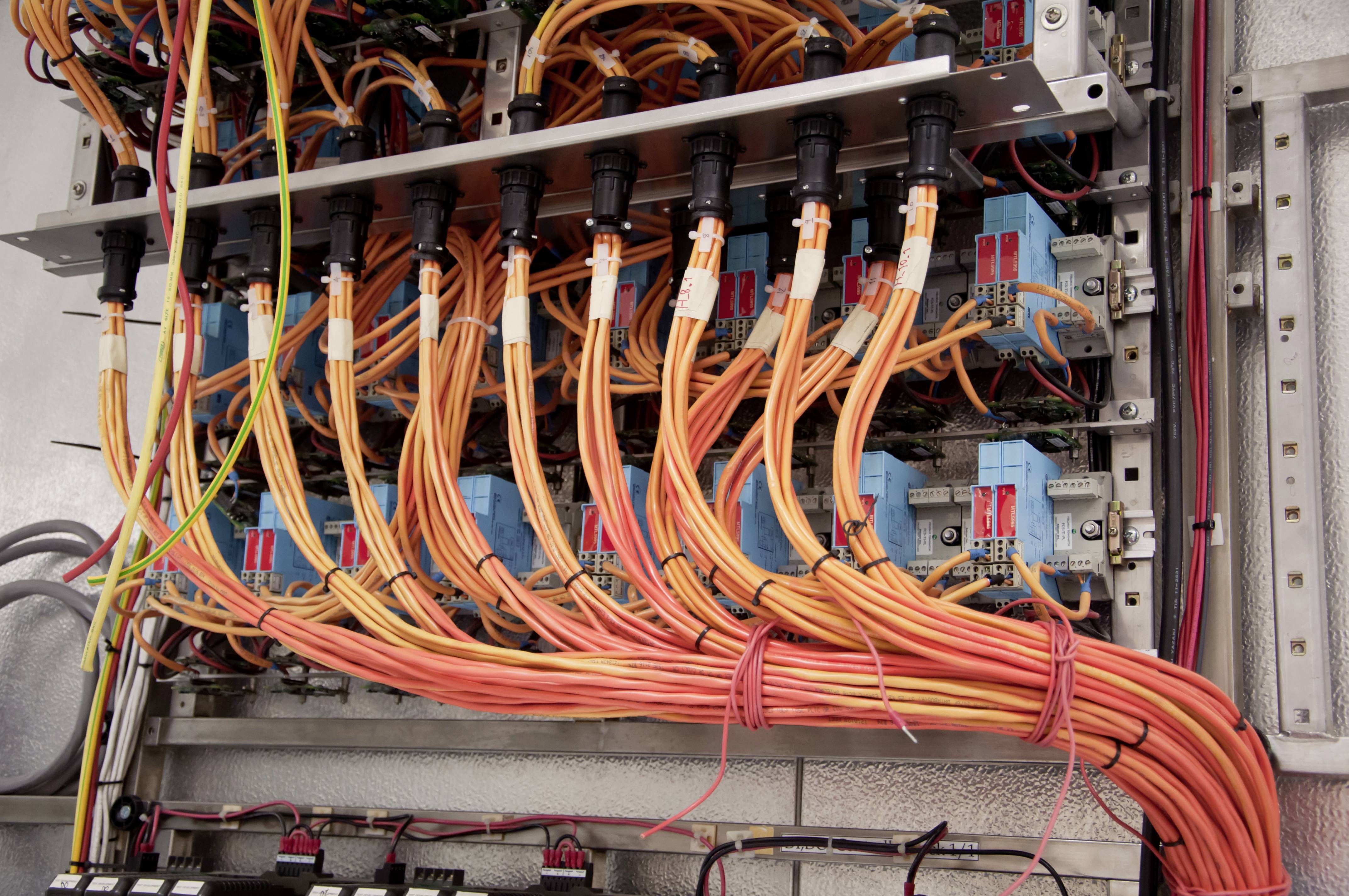 Een schakelkast vol oranje en gele kabels die zijn aangesloten op connectoren toont de complexiteit van een elektrische installatie.