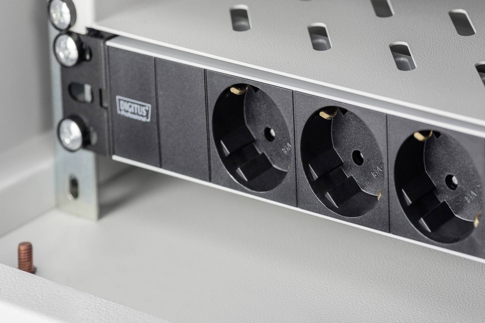 Een zwart stekkerdoosmodule met drie geaarde stopcontacten is ingebouwd in een grijs metalen rek.