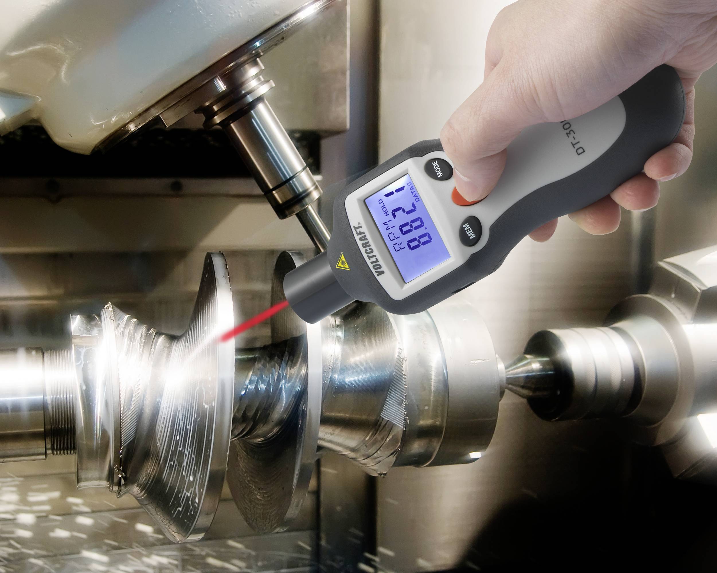 Een handapparaat meet de rotatiesnelheid van een roterende metalen machine met een rode laserstraal. Het display toont '7280'.