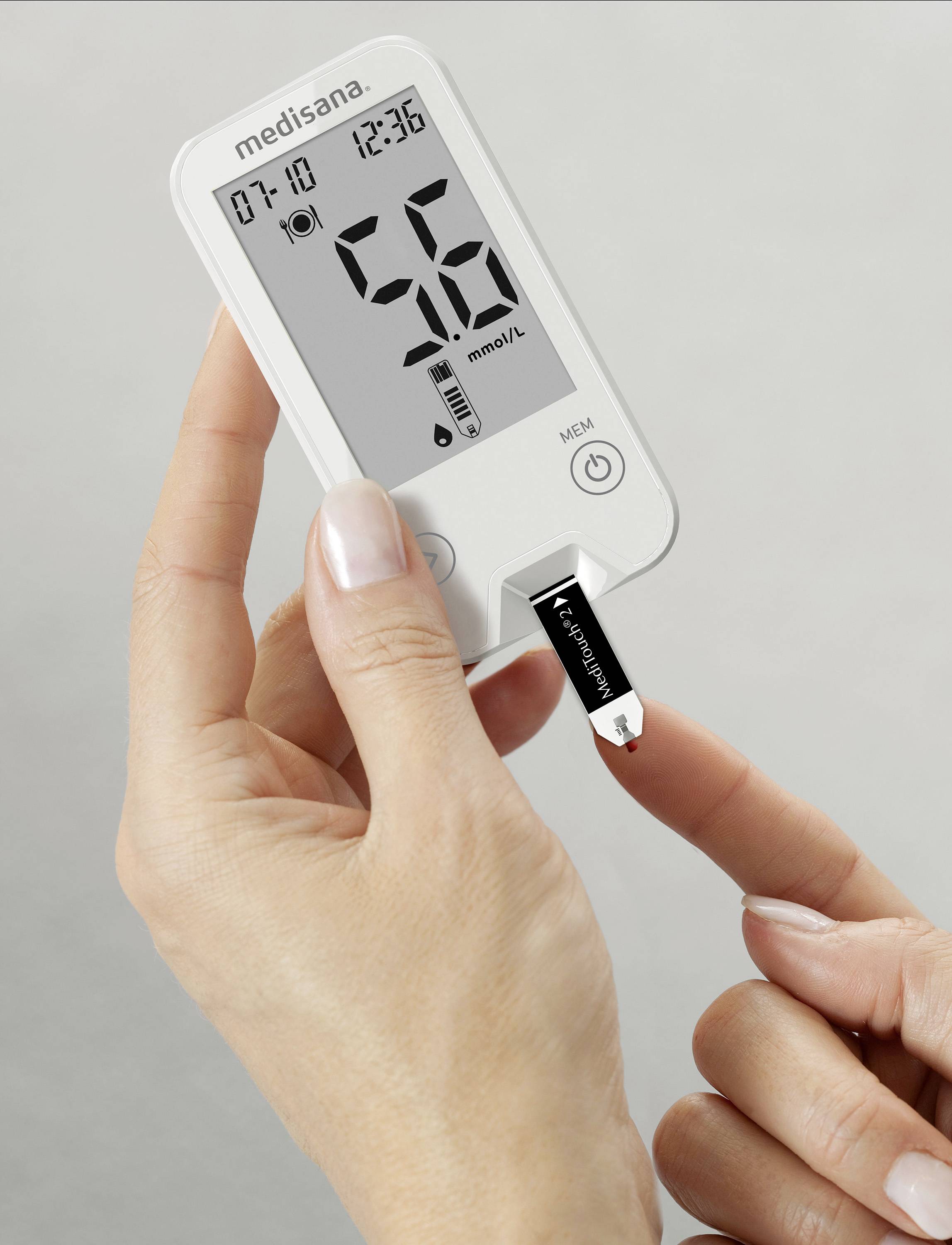 Een hand houdt een bloedglucosemeter vast met een teststrip. Het scherm toont '56 mmol/L', datum en tijd.