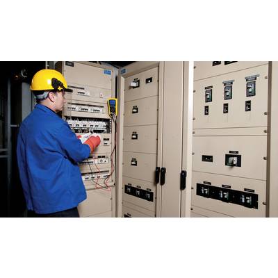 Een elektricien in blauwe werkkleding en een gele helm controleert schakelkasten met een multimeter in een controlekamer.