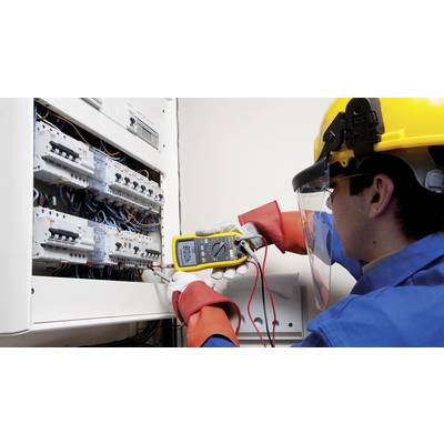 Een technicus met veiligheidshelm controleert de elektrische schakelkast met een multimeter.