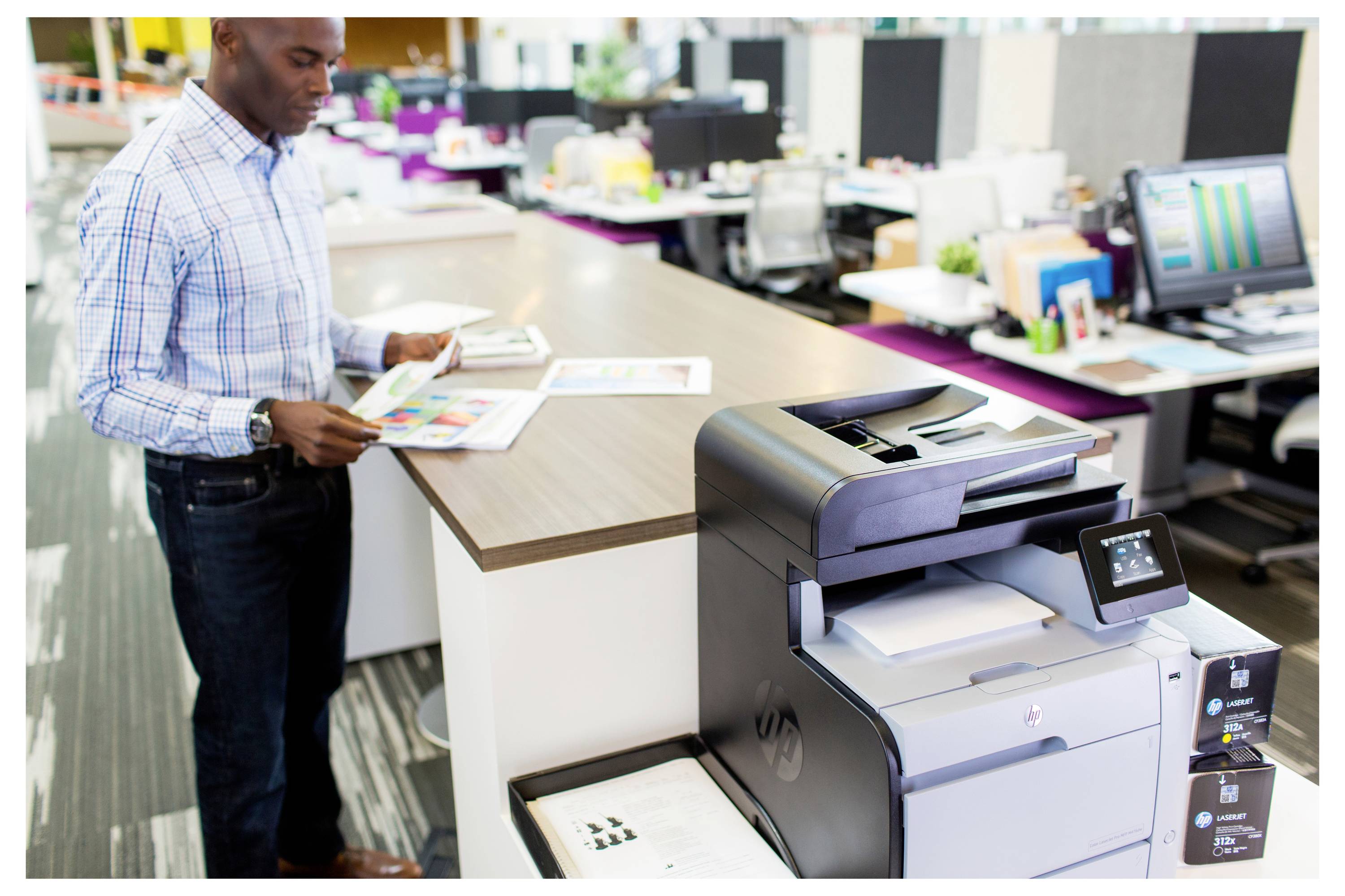 Kantoormedewerker die documenten controleert naast een grote multifunctionele printer/kopieerapparaat op een druk kantoorwerkplek.