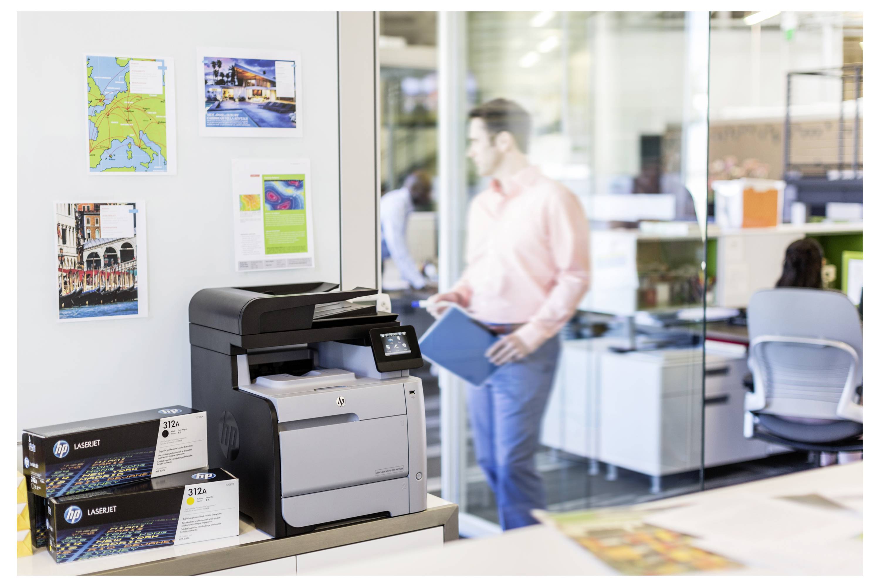 Kantoorkantoorhal met een HP LaserJet-printer op een balie en een vage man met een map op de achtergrond.