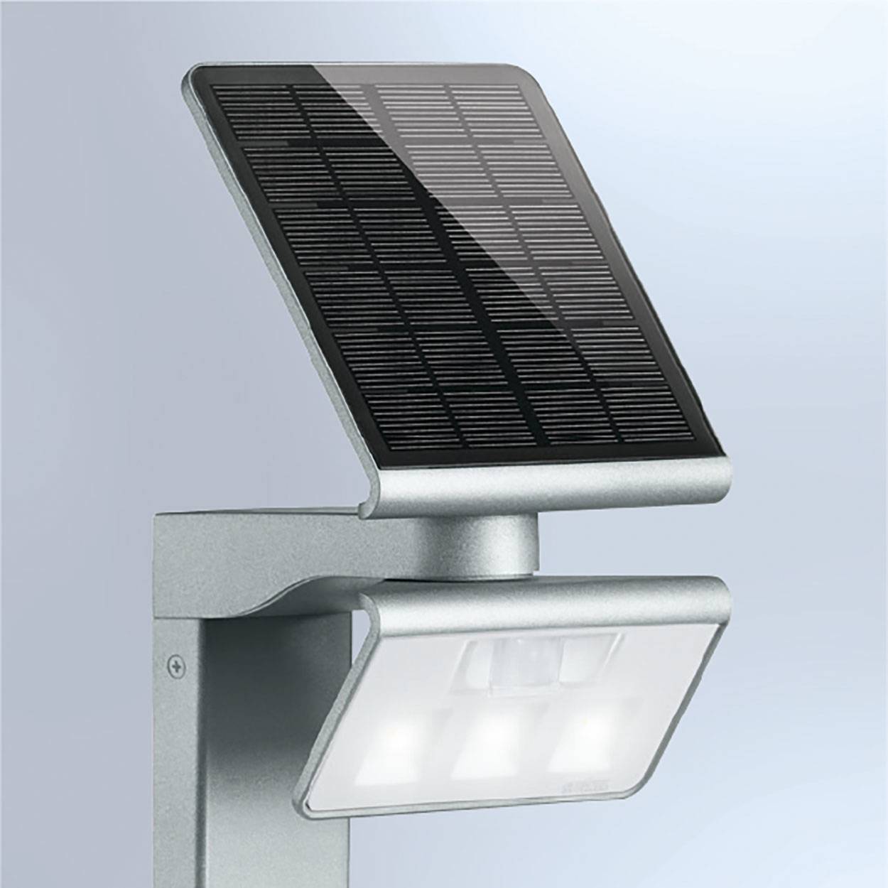 Een zilveren, wandgemonteerde solarlamp met een zonnepaneel bovenaan en drie LED's onderaan. Hij geeft helder licht.