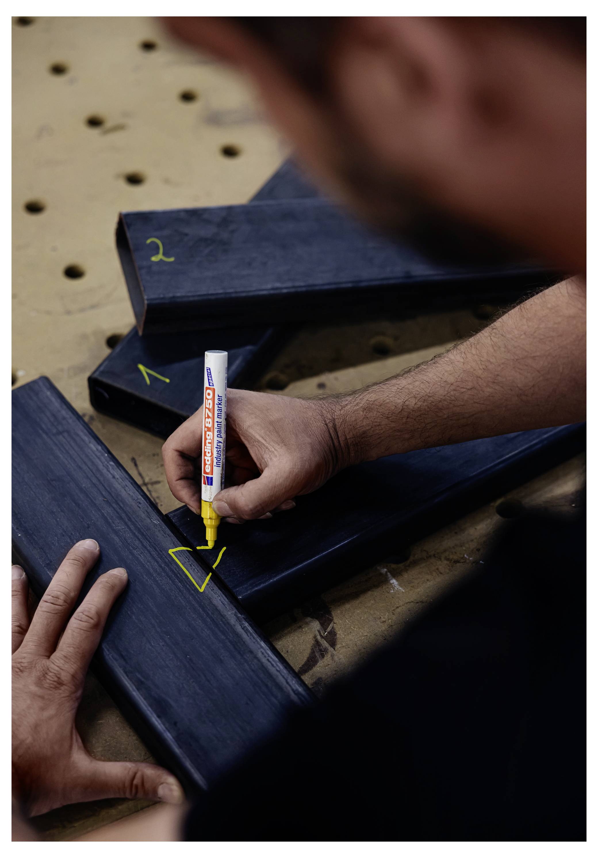 Persoon die donkere houten planken met een gele marker op een werkbank markeert, waarschijnlijk voor het meten of labelen van stukken voor montage.