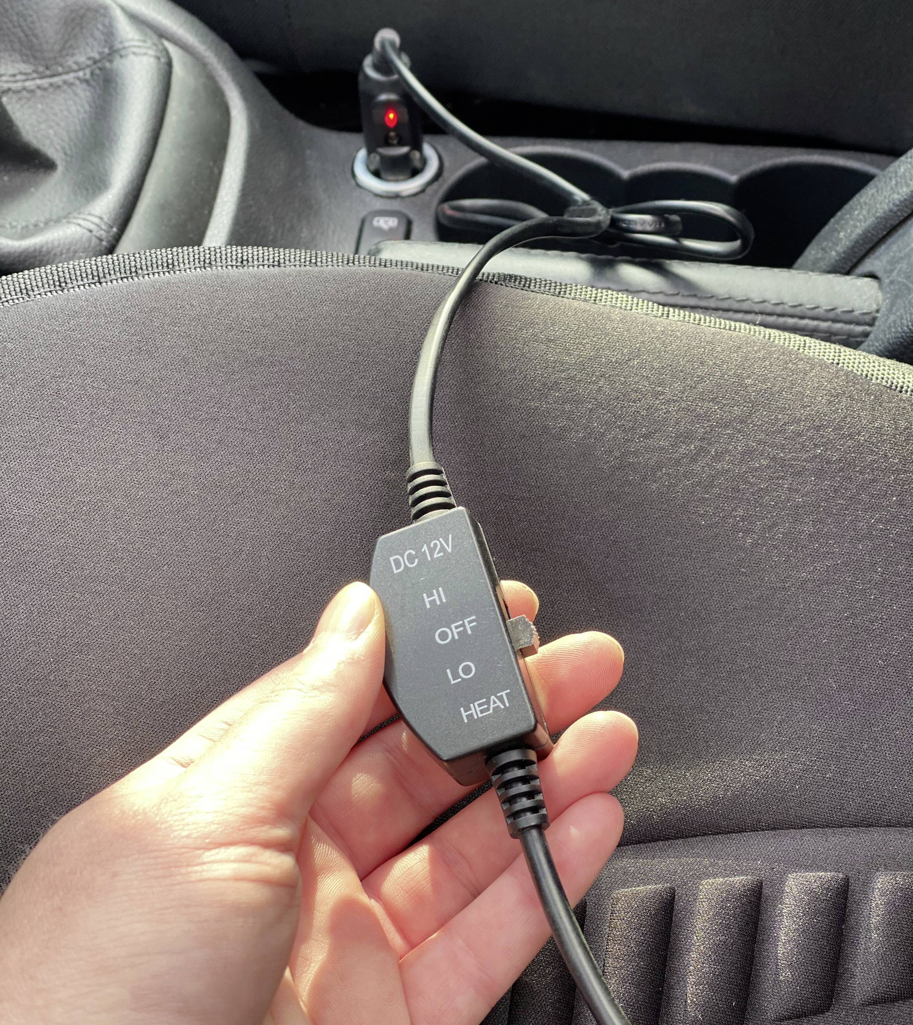 'Persoon houdt schakelaar van een 12V-verwarmingskussen in de auto vast. Schakelaar toont opties: HI, UIT, LO.'
