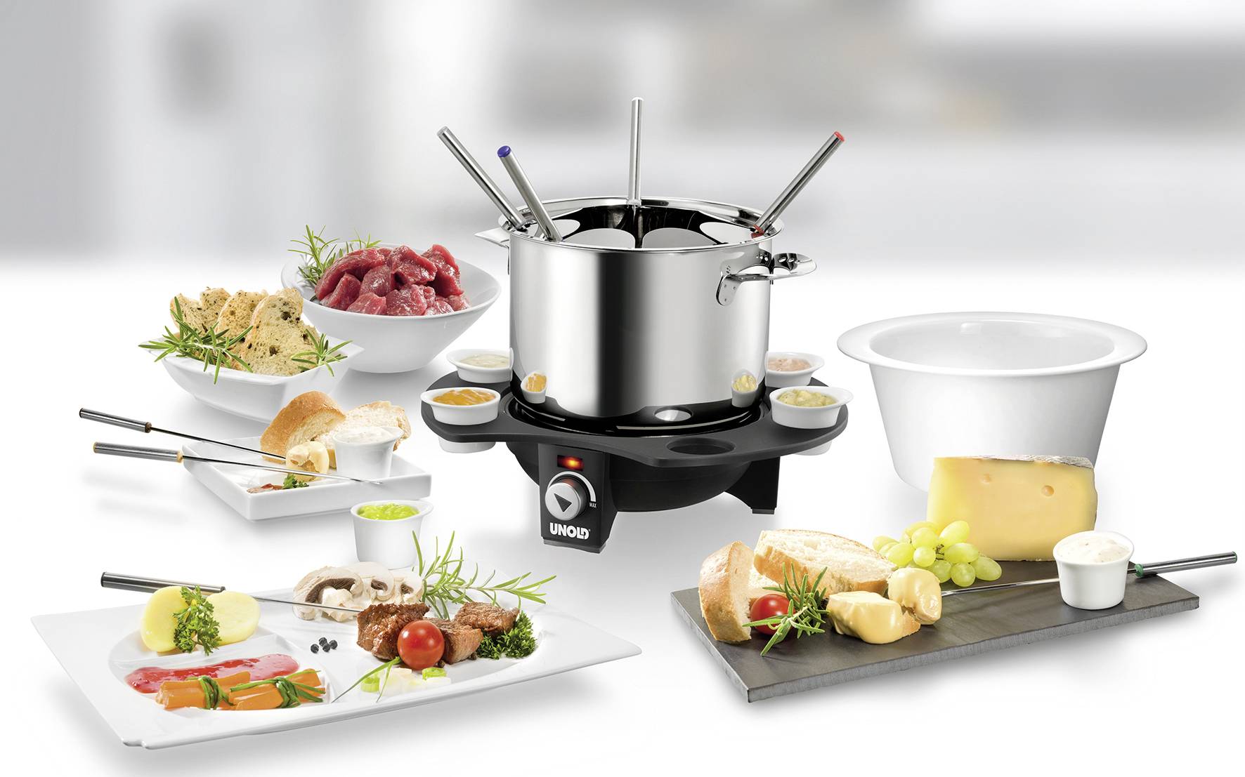 Een fondueset met acht vorken, omringd door vlees, brood, kaas, druiven en sauzen op borden.