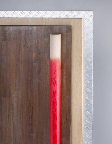 Een houten stok die gedeeltelijk rood is gelakt, staat rechtop tegen een muur en wordt omgeven door een metalen frame.